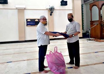 Yusrin Deu selaku Ketua Takmirul Masjid Agung Baiturrahim, saat membagikan sajadah kepada jamaah.