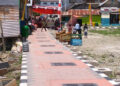 Di atas paving yang baru terpasang, warga Kelurahan Lekobalo berjalan menuju tenda syukuran, Rabu (22/4/2026). Perayaan sederhana itu menjadi ungkapan syukur atas berkurangnya genangan air saat hujan. Namun di balik suasana yang nyaris seperti hari raya, proyek penataan kawasan tersebut belum sepenuhnya rampung—sejumlah pekerjaan fisik masih berlangsung, sementara persoalan pembayaran antar pihak pelaksana belum juga tuntas. Foto: Lukman/mimoza.tv.