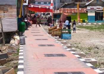 Di atas paving yang baru terpasang, warga Kelurahan Lekobalo berjalan menuju tenda syukuran, Rabu (22/4/2026). Perayaan sederhana itu menjadi ungkapan syukur atas berkurangnya genangan air saat hujan. Namun di balik suasana yang nyaris seperti hari raya, proyek penataan kawasan tersebut belum sepenuhnya rampung—sejumlah pekerjaan fisik masih berlangsung, sementara persoalan pembayaran antar pihak pelaksana belum juga tuntas. Foto: Lukman/mimoza.tv.