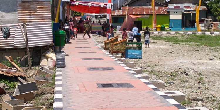 Di atas paving yang baru terpasang, warga Kelurahan Lekobalo berjalan menuju tenda syukuran, Rabu (22/4/2026). Perayaan sederhana itu menjadi ungkapan syukur atas berkurangnya genangan air saat hujan. Namun di balik suasana yang nyaris seperti hari raya, proyek penataan kawasan tersebut belum sepenuhnya rampung—sejumlah pekerjaan fisik masih berlangsung, sementara persoalan pembayaran antar pihak pelaksana belum juga tuntas. Foto: Lukman/mimoza.tv.