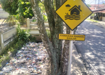 Rambu “Kawasan Rawan Banjir” berdiri tegak di Jalan Cendrawasih, Kota Gorontalo, namun saluran drainase di sisinya justru dipenuhi sampah. Ironi yang mencerminkan masih rendahnya kesadaran lingkungan, sekaligus menjadi ancaman nyata bagi potensi banjir di kawasan tersebut. Foto: Lukman/mimoza.tv